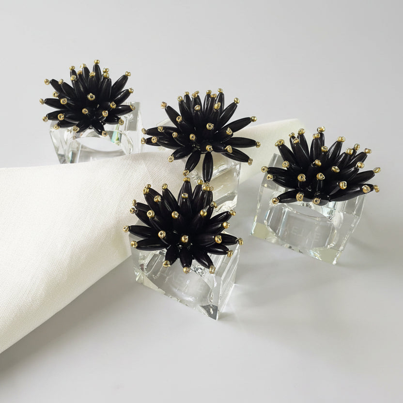 Hand-beaded black napkin rings with a floral design on a lucite base, adding elegant flair to table settings.