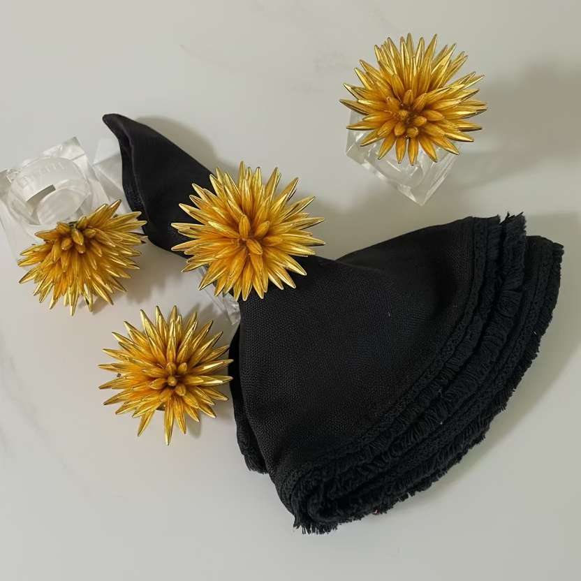 Hand-beaded gold napkin rings with a floral design on a lucite base, adding luxury to table settings.