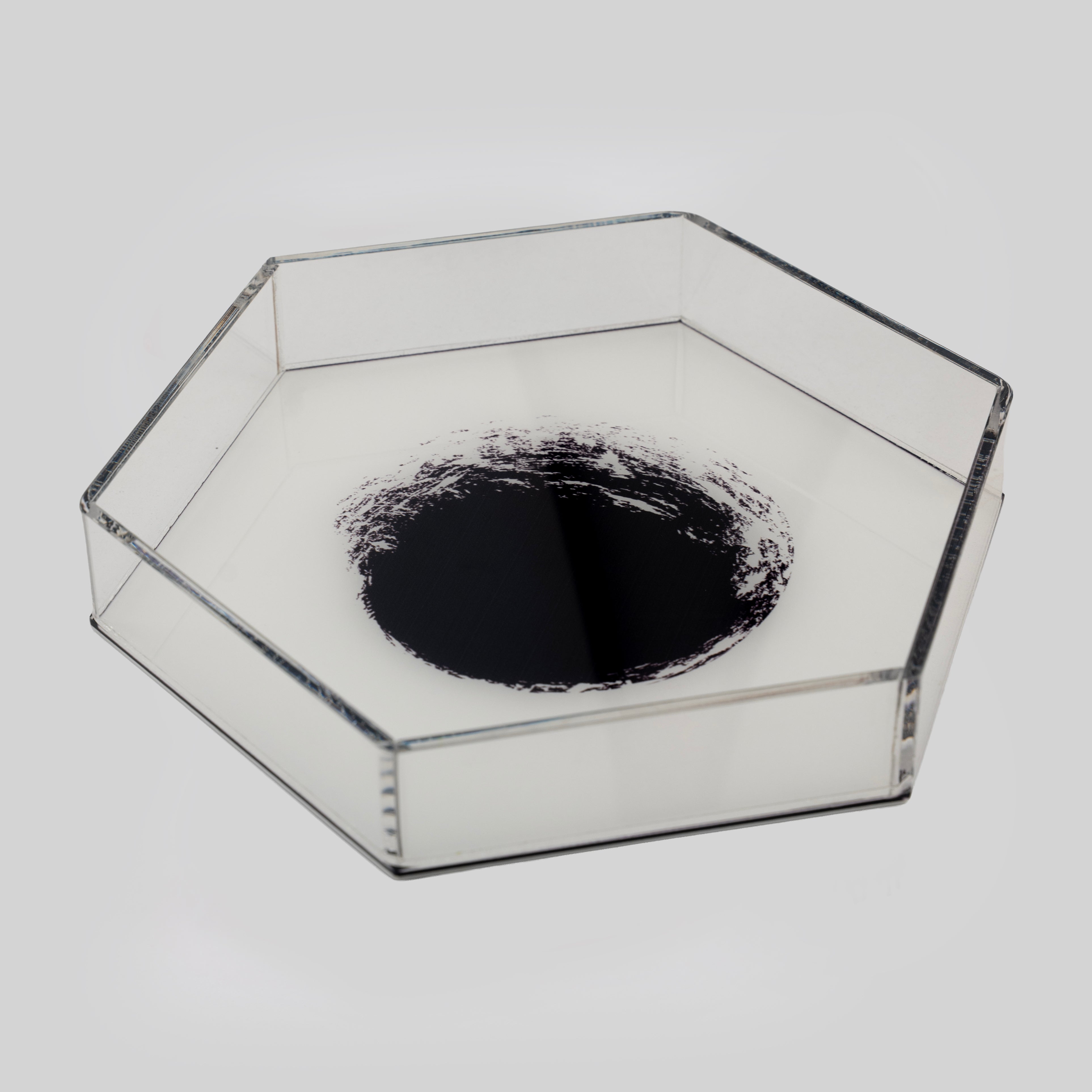Hexagonal clear acrylic tray with a dramatic black ink cosmos nebula print at the centre, feathering outward into white — shot at an angle on a grey background.