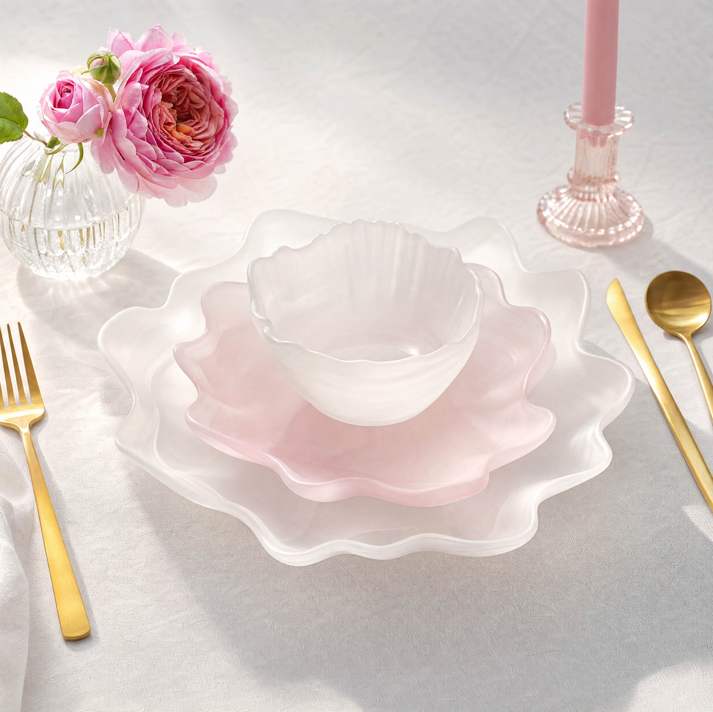 "Tyetye wavy-edge tableware set — white and pink scalloped dinner plates with matching bowl, styled with pink garden roses, gold cutlery, and a pink glass candlestick on white linen"
