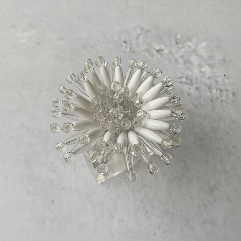 Hand-beaded white napkin rings designed to resemble blooming flowers, set on a lucite base, enhancing elegant table settings.